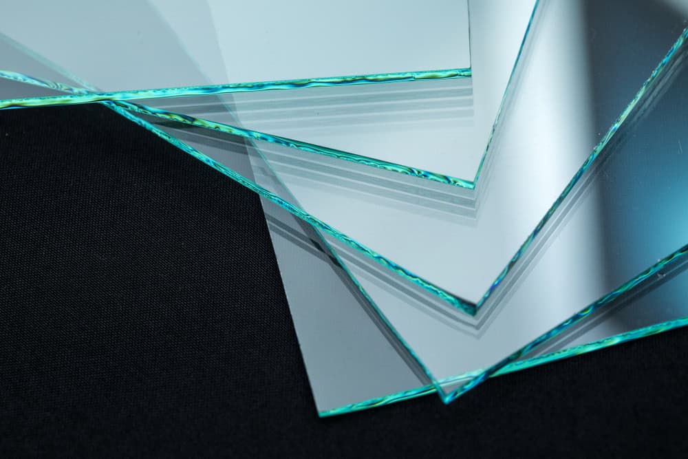 Close-up image of several overlapping transparent glass sheets with green-tinted edges, arranged in a slightly fanned-out pattern. The background is solid black, providing contrast to the glass—a stunning example of Architectural Glass Litchfield County craftsmanship.
